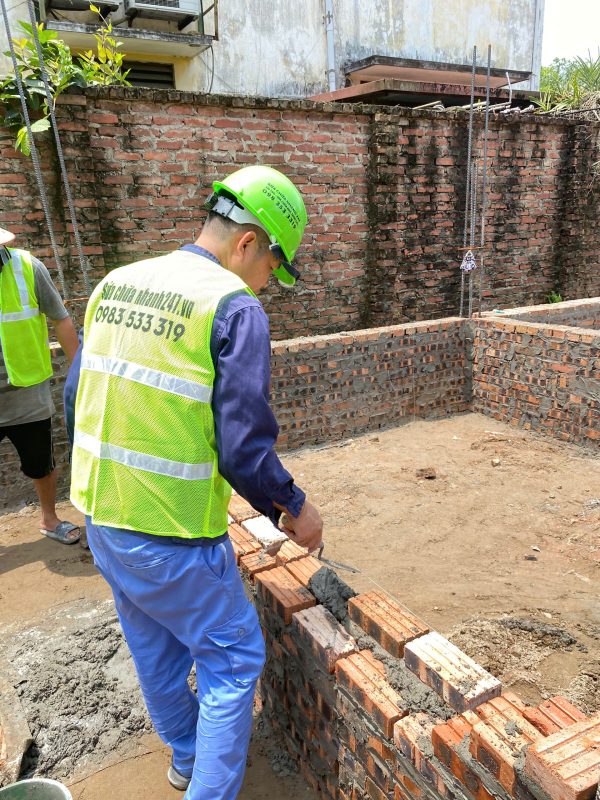 Thợ thi công đang cầm bay lấy vữa xi măng - cát và trải đều lên mặt lớp gạch vừa xây.