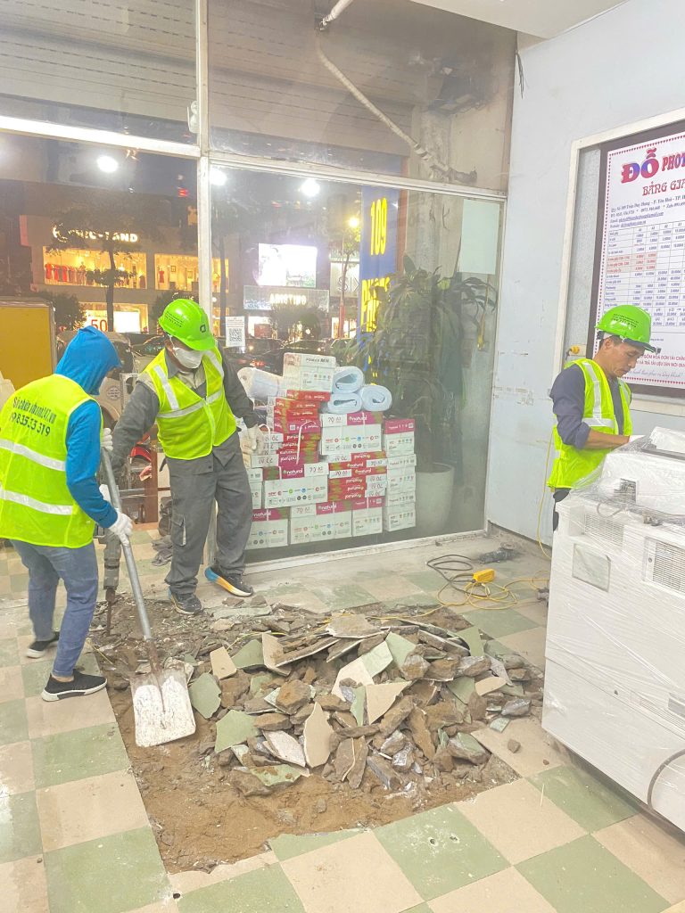Nhóm thợ đang phối hợp thực hiện công đoạn phá dỡ và dọn dẹp nền gạch cũ trong cửa hàng photocopy,