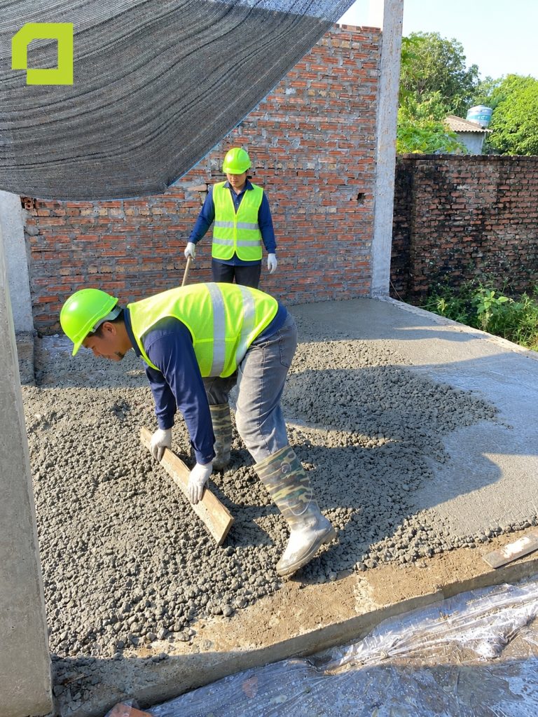 Hai người thợ thi công đang thực hiện công đoạn cán phẳng bề mặt bê tông sàn/nền.